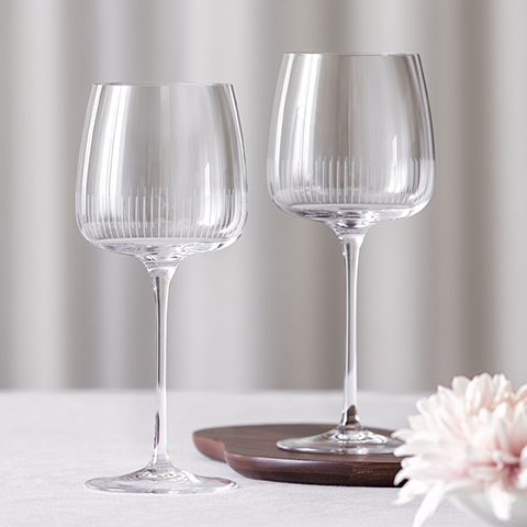 Un arrangement élégant de trois verres à cocktail élégants sur une table sombre avec un vase en céramique contenant des branches feuillues. Chaque verre contient une boisson claire et des garnitures. La scène est éclairée chaleureusement et possède un fond doré.