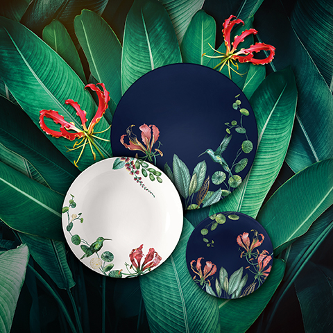 Sur une table ronde et réfléchissante se trouvent une bougie allumée, une tasse de café avec sa soucoupe et une cuillère dorée, un bol de biscuits saupoudrés de sucre glace, un sucrier, un pot à crème et un vase d'orchidées roses et blanches.