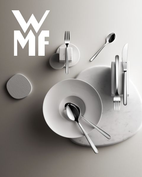 Une cocotte remplie de figues, de mûres et de garnitures aromatiques est posée sur une planche de bois sombre. Au-dessus de la cocotte, on aperçoit le logo WMF. L'arrière-plan est une surface sombre texturée.