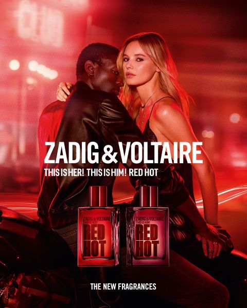 Femme aux longs cheveux roux et tenue noire assise sur un lit dans une pièce avec une cage à oiseaux et une grande fenêtre. Texte : « Zadig & Voltaire » et « Zadig : Le nouveau parfum rechargeable ». Logo avec des ailes et un fer à cheval.