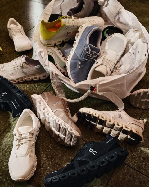 Une multitude de chaussures de course On de différentes couleurs sont éparpillées sur le sol, débordant d'un sac fourre-tout blanc, exhibant leurs semelles rembourrées distinctives.