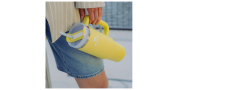 Personne en short en jean tenant une grande tasse jaune avec anse et paille, et portant une veste claire.