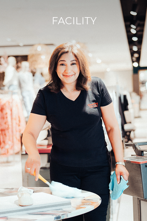 Une femme en chemise noire nettoie en souriant une table avec un plumeau et un chiffon dans un magasin moderne et lumineux. Au-dessus d'elle apparaît le mot "INSTALLATION".
