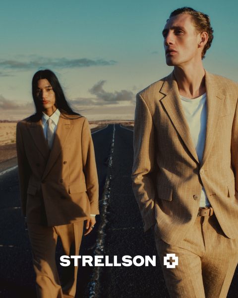 Un homme et une femme en élégants costumes marron marchent dans une rue vide au coucher du soleil. Le logo Strellson apparaît en bas de l'image.