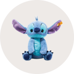 Ein Plüschtier von Stitch aus Disneys "Lilo & Stitch" mit großen blauen und lilafarbenen Ohren, großen Augen und einem Steiff Anhänger im linken Ohr auf einem hellen runden Hintergrund.