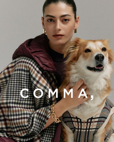 Une femme portant un manteau à carreaux et des accessoires dorés pose avec un chien beige et blanc portant une tenue à carreaux assortie. Le mot « COMMA » apparaît en grandes lettres blanches sur l'image.