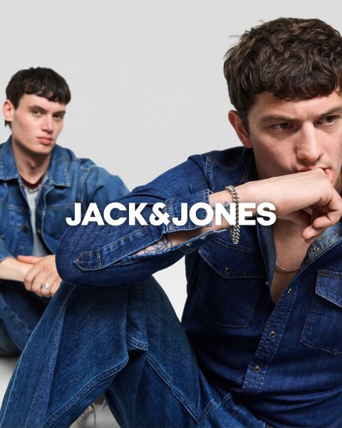 Deux hommes en tenue de jeans sont assis devant un fond simple. L'homme de devant porte sa main à sa bouche, tandis que l'autre est assis derrière lui. Au centre, on peut lire le texte "JACK & JONES".