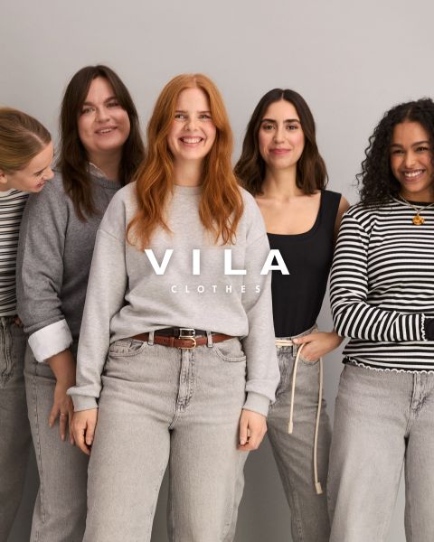 Cinq femmes en tenues décontractées, notamment des jeans et des hauts de couleurs neutres, se tiennent proches les unes des autres et sourient devant un fond uni. Le texte superposé est "Vila Clothes".