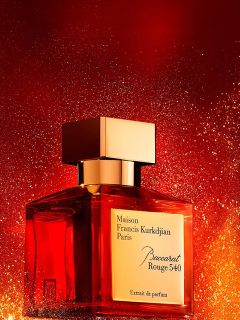 Un flacon du parfum Maison Francis Kurkdjian Paris Baccarat Rouge 540 avec un capuchon doré se dresse devant un fond rouge et or éclatant.