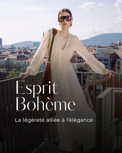 Eine Frau in einem fließenden cremefarbenen Kleid und mit Sonnenbrille steht auf einem Balkon mit Blick auf eine Stadt und die Berge im Hintergrund. Der Text lautet "Esprit Bohème".