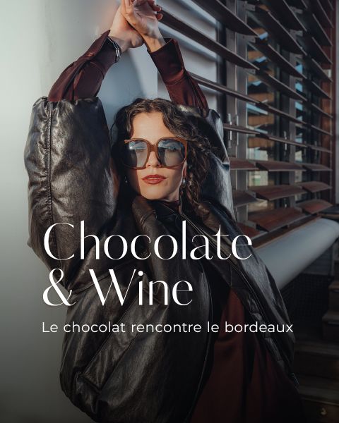 Une femme élégante avec des lunettes de soleil et une veste sombre s'appuie contre un bâtiment moderne. Le texte sur l'image est : "Chocolat et vin. Le chocolat rencontre le bordeaux."