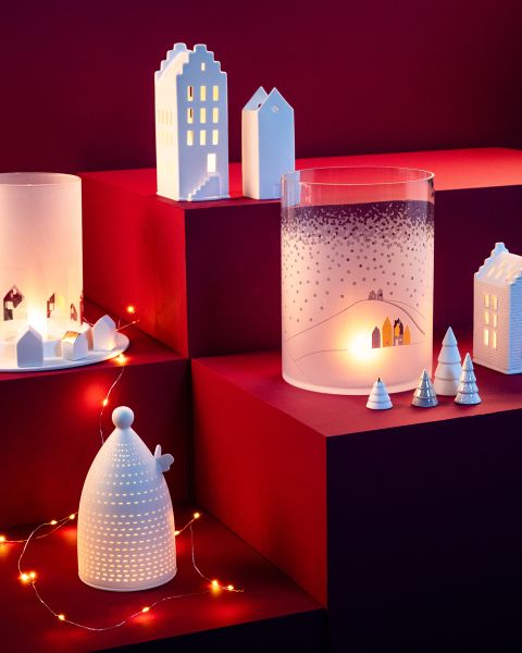 Des maisons en céramique, des arbres et des bougeoirs sont disposés sur des marches rouges et sont doucement éclairés par des guirlandes lumineuses et la lumière des bougies. La scène rappelle une atmosphère de village d'hiver chaleureuse et festive.