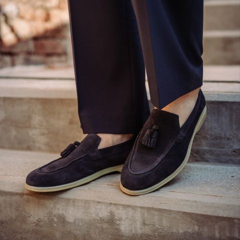 Une personne portant des chaussures en daim noir à glands et un pantalon foncé se tient sur un escalier extérieur en béton.