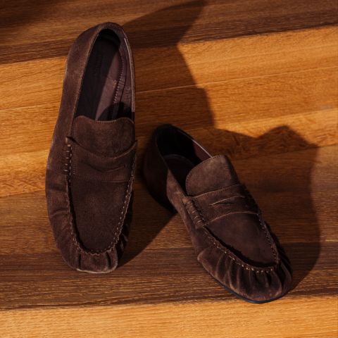 Une paire de chaussures en daim marron, exposées sur des marches en bois, dont la texture est mise en valeur par l'ombre et la lumière.