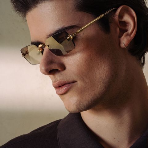 Homme avec des lunettes de soleil à monture dorée et une chemise foncée.