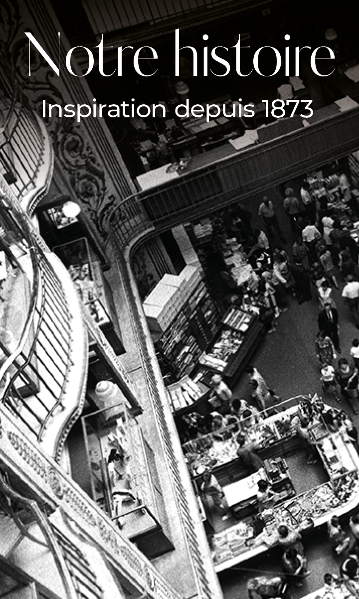 Photo en noir et blanc d'un grand magasin animé à plusieurs étages rempli de clients. Des balcons incurvés surplombent la scène. Le texte superposé en français se lit comme suit : "Notre histoire, une inspiration depuis 1873".