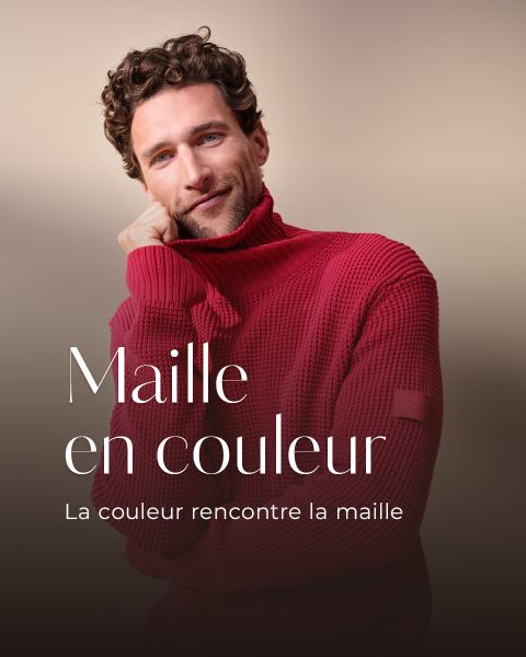 Un homme aux cheveux bouclés porte un pull à col roulé rouge et sourit doucement en posant sa main sur son visage. Texte français : "Maille en couleur. La couleur rencontre la maille."
