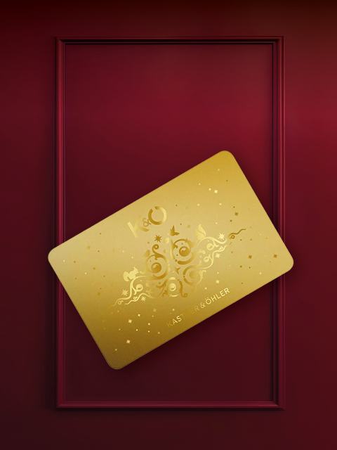 Une carte dorée avec un motif ornemental et les lettres "K&O" est placée en biais sur un fond bordeaux avec un cadre rectangulaire.