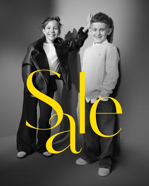Deux enfants souriants posent dans des tenues chics avec le mot « Sale » en grandes lettres jaunes au-dessus de l'image.