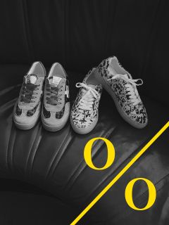 Une photo en noir et blanc de deux paires de baskets à motifs sur un siège en cuir noir. Une ligne diagonale jaune avec deux lettres "O" jaunes orne le coin inférieur droit de l'image.