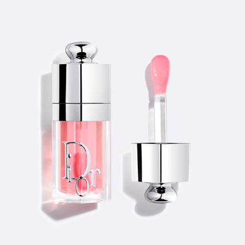 Un tube de gloss Dior avec un brillant rose et un capuchon argenté, présenté ouvert avec l'applicateur à côté sur un fond blanc.