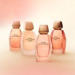 Quatre flacons du parfum « All of Me » de Narciso Rodriguez dans des tons délicats de rose et de beige, arrangés devant un fond clair et légèrement flou.