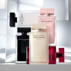 Cinq flacons de parfum de Narciso Rodriguez en noir, blanc, rose et rouge sont dressés et empilés devant un fond moderne et réfléchissant.