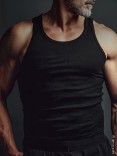 Un homme musclé avec une barbe grise porte un débardeur noir et se tient devant un fond sombre. Son visage est partiellement hors du cadre.