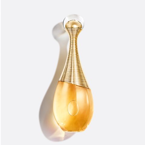 Élégant flacon de parfum doré au design incurvé et au bouchon rond et transparent sur un fond clair avec des ombres douces.