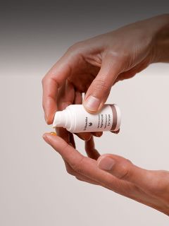 Une personne dépose une petite quantité de crème ou de lotion d'une bouteille blanche sur le bout de son doigt.