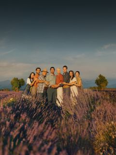 Un groupe de huit personnes se tient la main dans un champ de lavande sous un ciel clair, entouré de fleurs violettes en fleurs.