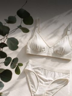 Un ensemble crème de soutien-gorge et culotte repose sur une surface claire, sur laquelle tombent des ombres de feuilles.