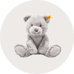 Ein weicher, grauer Plüschbär mit einem gelben Anhänger im Ohr, der aufrecht vor einem schlichten, hellen Hintergrund sitzt.