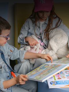 Deux enfants en vêtements en jean lisent ensemble un livre coloré, l'un tenant un lapin en peluche et l'autre pointant une page.