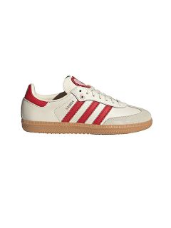 Basket blanche avec des rayures et un talon rouges, une semelle en caoutchouc marron clair et le texte "SAMBA" sur le côté. Design Adidas classique sur un fond blanc uni.