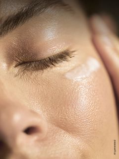 Un gros plan du visage d'une personne aux yeux fermés, montrant une peau lisse et éclatante et une touche de crème sous l'œil.