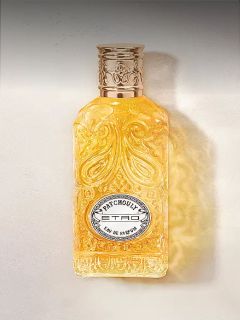 Flacon en verre orné contenant un liquide doré, avec un motif en relief et une étiquette argentée portant l'inscription "Patchouly TRD Eau de Parfum".