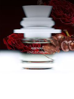 Un flacon de parfum en verre portant l'inscription "LOVE EXTREME" avec un effet de mouvement flou, devant des roses rouges et un fond sombre.
