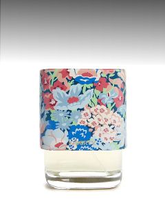 Un flacon de parfum en verre avec un bouchon coloré à motifs floraux devant un fond gris dégradé.