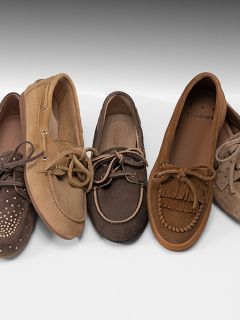 Quatre paires de chaussons et de mocassins marron et beige pour femmes, avec différentes textures et détails, disposés côte à côte sur une surface blanche.