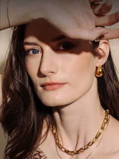 Femme à la peau claire et aux cheveux bruns, portant des bijoux en or et tenant sa main au-dessus de ses yeux, dont l'un est bleu et l'autre marron.