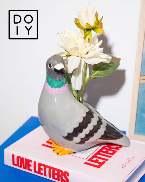 Vase colombe en céramique avec des fleurs blanches sur un livre "Lettres d'amour", avec un logo DOIY dans le coin supérieur gauche.