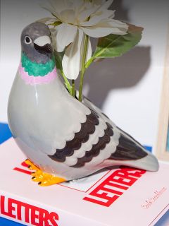 Une figurine de colombe en céramique avec une fleur blanche est posée sur un livre intitulé "LETTERS" avec une couverture blanche et rouge.