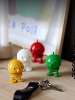 Quatre figurines de jouet rondes et colorées sont posées sur un bureau à côté de clés et d'un carnet, avec une œuvre d'art encadrée floue en arrière-plan.