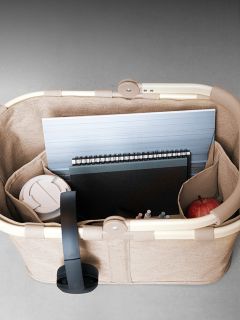 Un panier beige contient un ordinateur portable, un carnet, des stylos, une tasse de voyage blanche et une pomme rouge, vu de dessus.