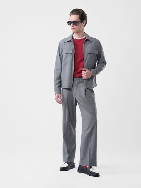 Homme avec des lunettes de soleil, un costume gris, une chemise rouge, des chaussures noires et blanches et un collier, devant un fond blanc.