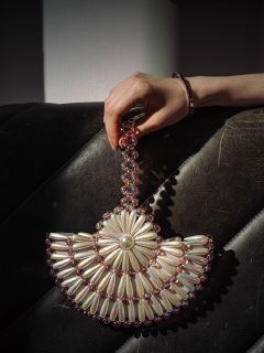 Une main tient un sac à main orné de perles avec des motifs de perles et de fleurs roses, reposant sur une surface en cuir noir texturé.