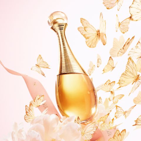 Flacon de parfum doré, entouré d'un ruban rose, de fleurs blanches et de papillons dorés flottants sur un fond pastel.