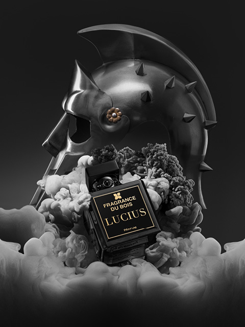 Au milieu de la fumée se trouve un flacon de parfum noir portant l'inscription « Fragrance Du Bois Lucius », avec un casque de gladiateur métallique visible en arrière-plan.