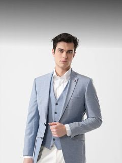 Homme en costume bleu clair avec une chemise blanche, debout devant un fond blanc uni, regardant la caméra avec assurance.